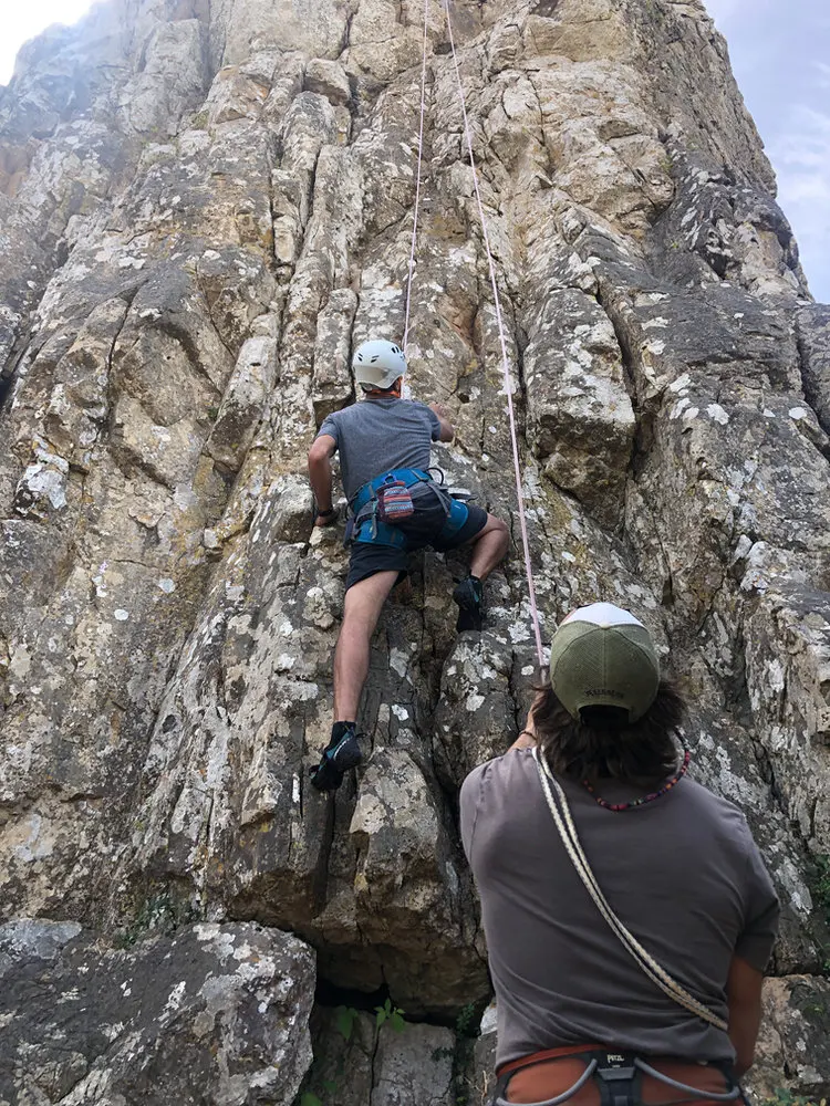 A helmeted climber and belayer at an outdoor rock face