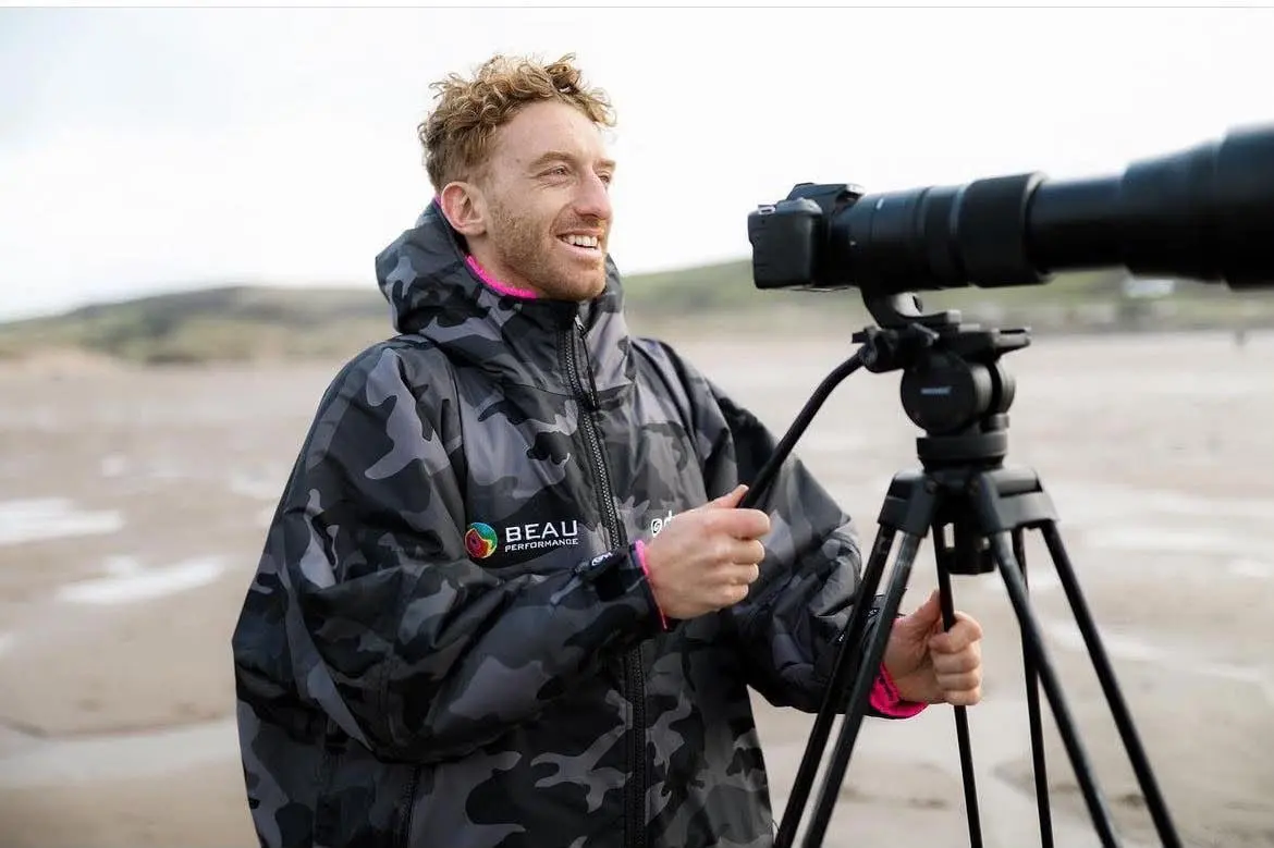 A surf coach beside a camera with a long telephoto lens