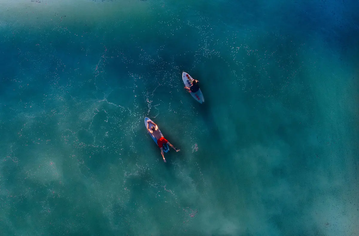 Two surfers paddling together in blue-green water