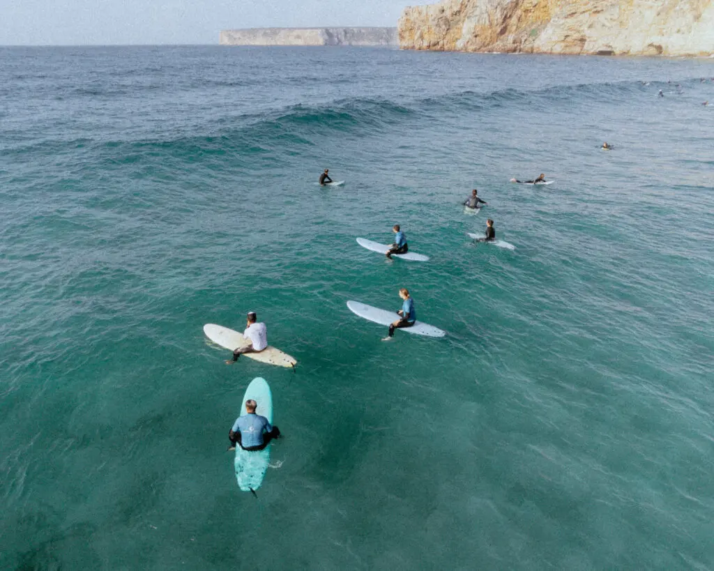 Surfers paddling towards a small wave below coastal cliffs