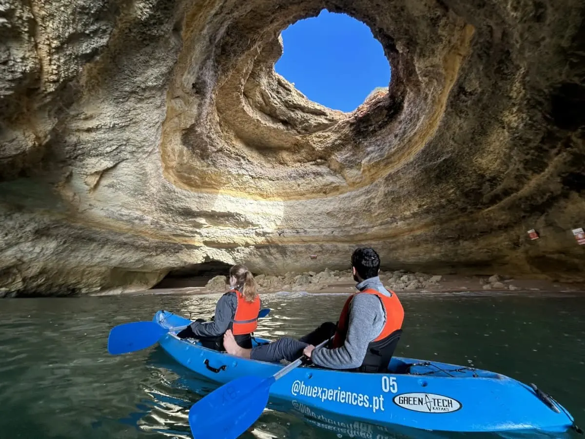 Two paddlers in a branded Blue Xperiences kayak under Benagil cave’s skylight