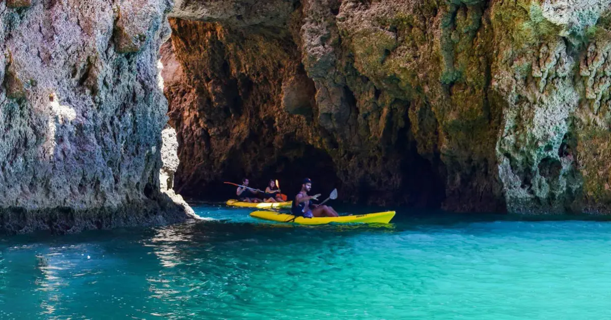 Kayakers paddle beside a rock arch on the Lagos coast