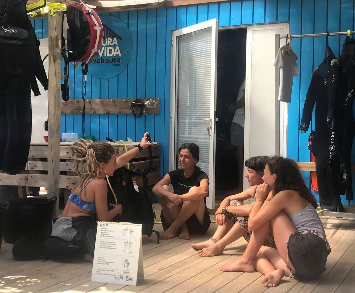 A small group studies diving equipment outside the blue PuraVida DiveHouse building