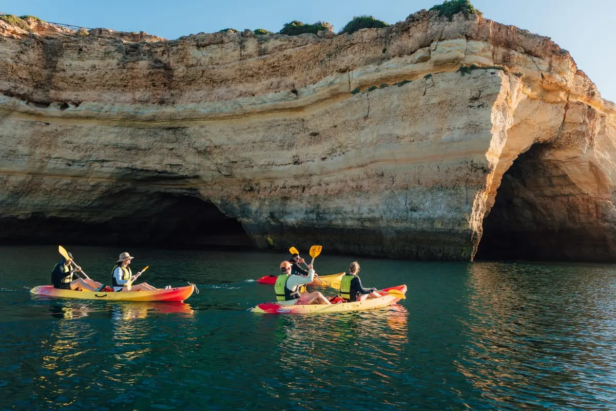 Kayakers wearing buoyancy aids below limestone cliffs near Benagil