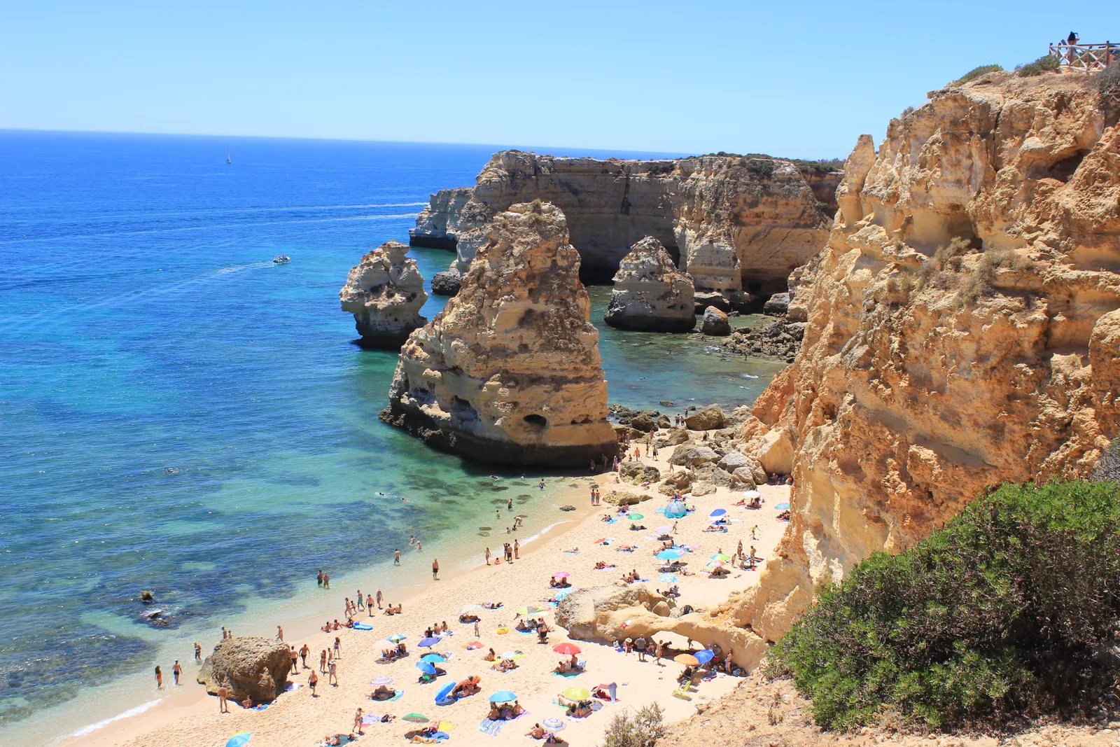Golden cliffs and sea stacks above the blue water and beach at Praia da Marinha